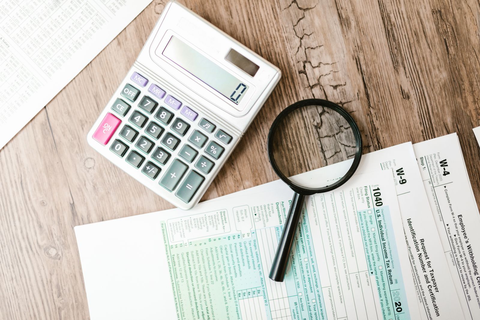 Tax forms laid out with a calculator and a magnifying glass on a wooden desk