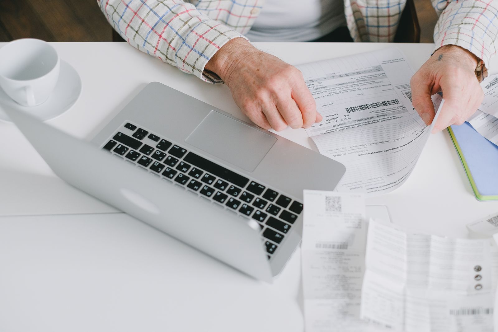 Hands sorting papers beside an open laptop