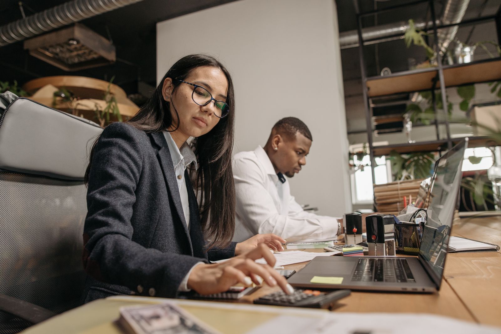 Two colleagues working on laptops and calculators in an office